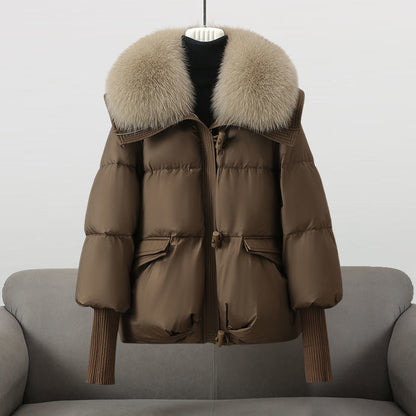 Braune Daunenjacke mit großem Pelzkragen, auf grauem Sofa präsentiert. Wintermode, warme Oberbekleidung, stilvolle Damenjacke.