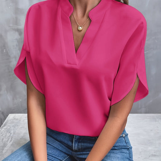Frau in pinker Bluse mit V-Ausschnitt und goldener Halskette, sitzt auf grauem Hintergrund. Modetrend, Damenmode, elegante Freizeitkleidung.