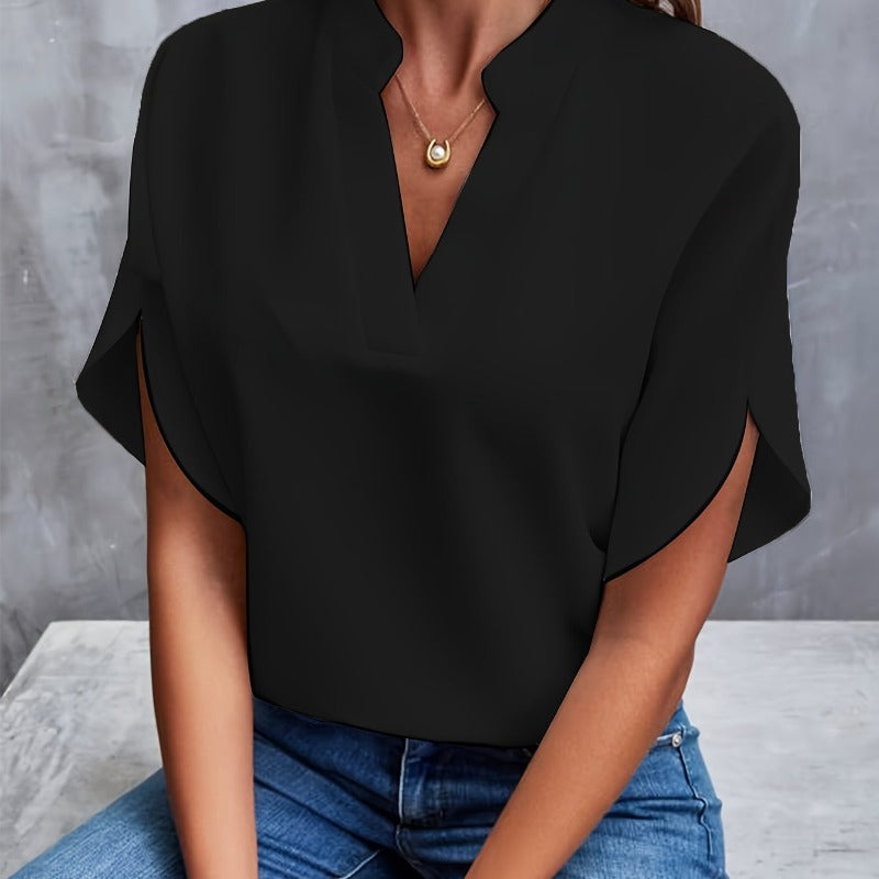 Frau in schwarzer Bluse mit V-Ausschnitt und goldener Halskette, sitzt auf grauem Hintergrund. Modetrend, elegante Damenbekleidung, Freizeitlook.