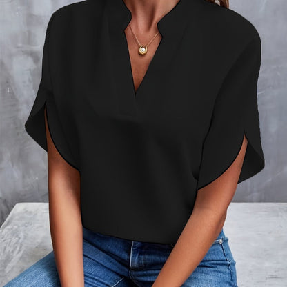Frau in schwarzer Bluse mit V-Ausschnitt und goldener Halskette, sitzt auf grauem Hintergrund. Modetrend, elegante Damenbekleidung, Freizeitlook.