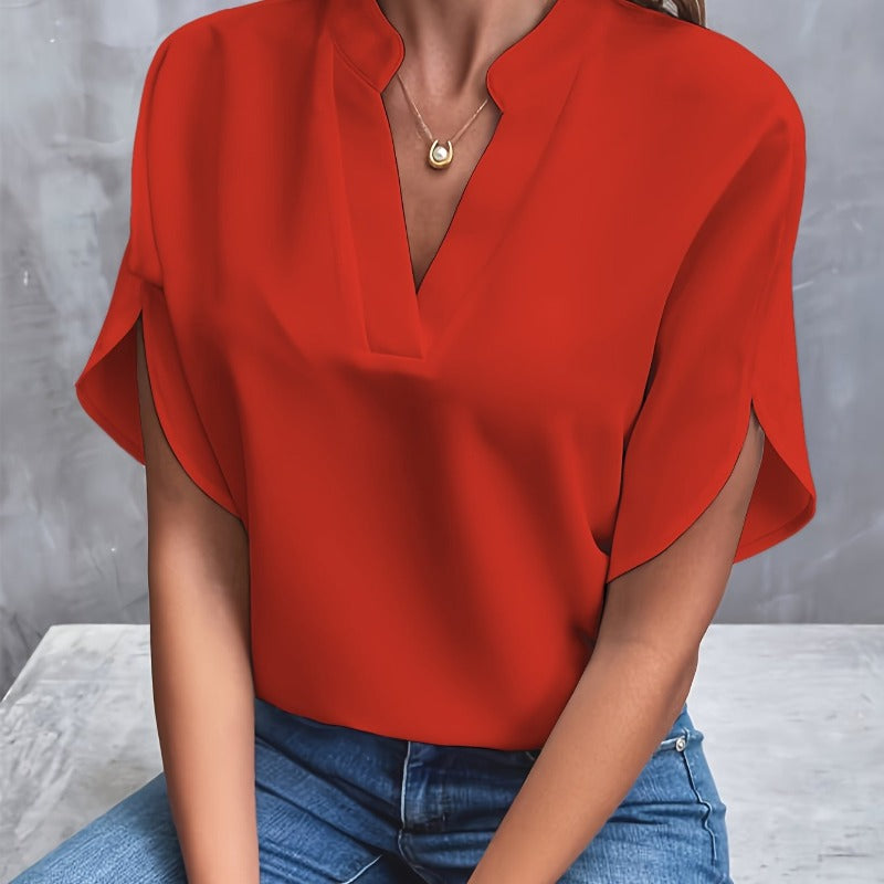 Frau in roter Bluse und blauer Jeans vor grauem Hintergrund, trägt goldene Halskette. Modetrend, elegante Damenbekleidung, Freizeitlook.