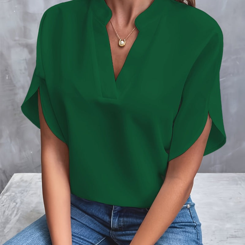Frau in grüner Bluse und blauer Jeans vor grauem Hintergrund, trägt goldene Halskette. Modetrend, Damenmode, lässiger Stil.