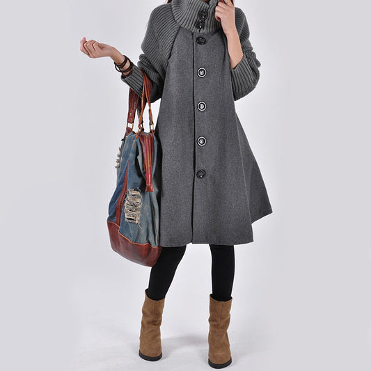 Frau in grauem Wollmantel mit großen Knöpfen, trägt braune Stiefel und eine große, bunte Tasche. Modischer Herbst-Look, stilvoll und elegant.