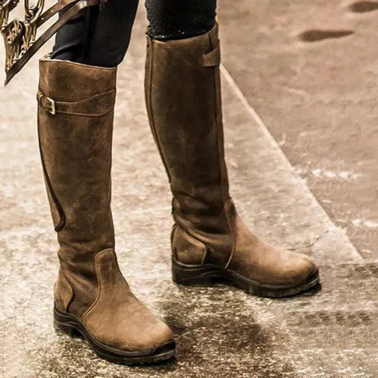 Braune Lederstiefel, kniehoch, mit Schnallen, auf nassem Asphalt. Modische Damenstiefel, ideal für Herbstmode und Outdoor-Aktivitäten.