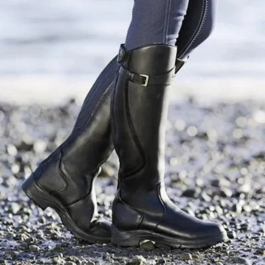 Schwarze Reitstiefel aus Leder auf Kieselsteinen am Strand. Hochwertige, wasserdichte Stiefel für Outdoor-Aktivitäten und Reitsport.
