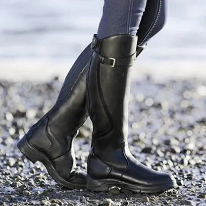 Schwarze Reitstiefel aus Leder auf Kieselsteinen am Strand. Hochwertige, wasserdichte Stiefel für Outdoor-Aktivitäten und Reitsport.