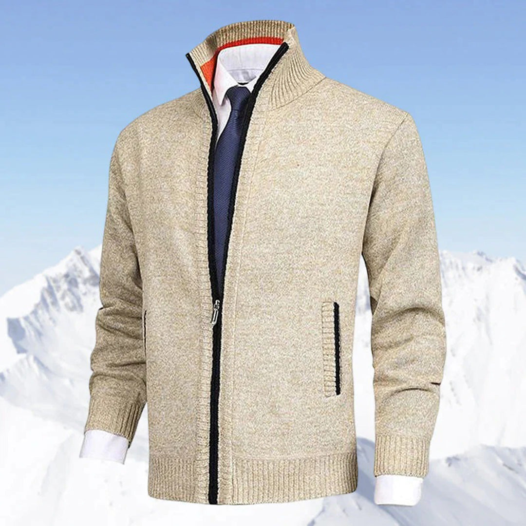 Beige Herrenjacke mit Reißverschluss, kombiniert mit weißem Hemd und blauer Krawatte, vor schneebedeckten Bergen. Elegante Wintermode.