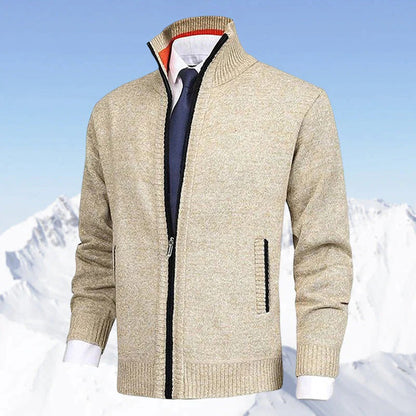 Beige Herrenjacke mit Reißverschluss, kombiniert mit weißem Hemd und blauer Krawatte, vor schneebedeckten Bergen. Elegante Wintermode.