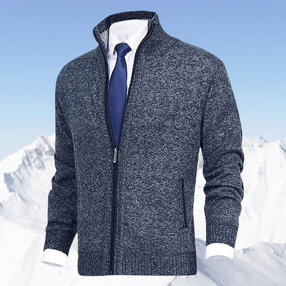 Grauer Herren-Strickpullover mit Reißverschluss, kombiniert mit weißem Hemd und blauer Krawatte, vor schneebedecktem Bergpanorama.