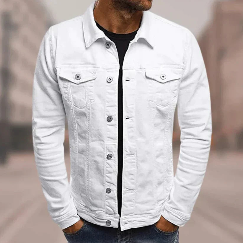 Mann in weißer Jeansjacke, schwarzem T-Shirt und blauer Jeans in urbaner Umgebung. Modetrend, Herrenbekleidung, lässiger Stil.