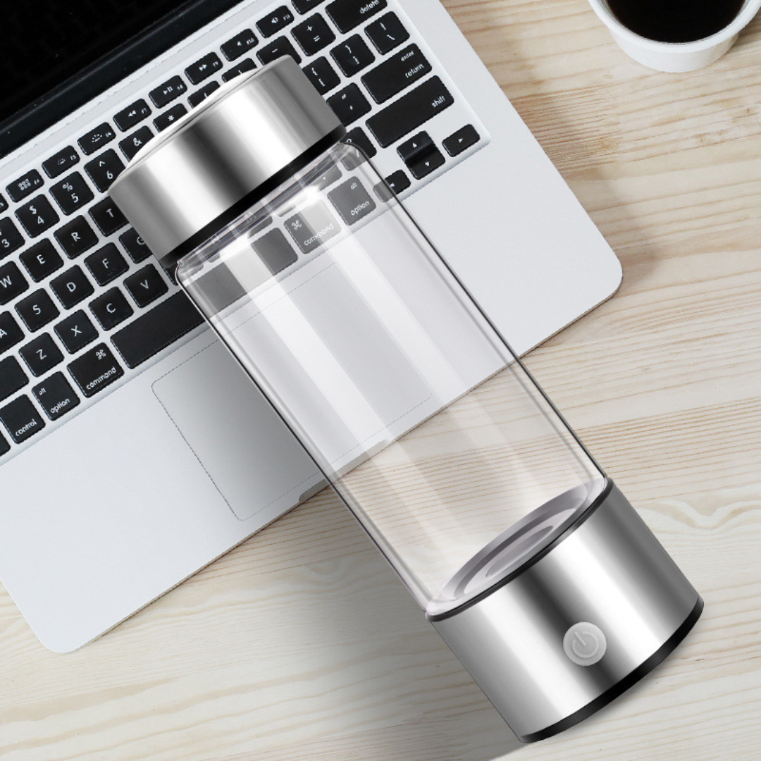 Transparente tragbare Wasserflasche mit silbernem Deckel auf Laptop und Holztisch. Ideal für Büro, Reisen, Fitness. Modernes, minimalistisches Design.