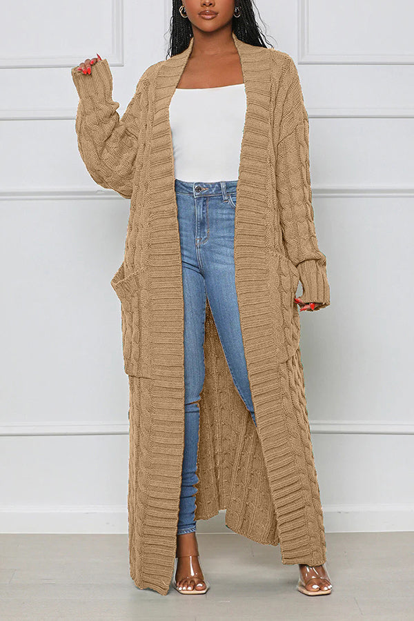 Frau trägt langen, beige Strick-Cardigan mit Zopfmuster, kombiniert mit weißem Top und blauer Jeans. Modetrend, Damenmode, Herbstoutfit.