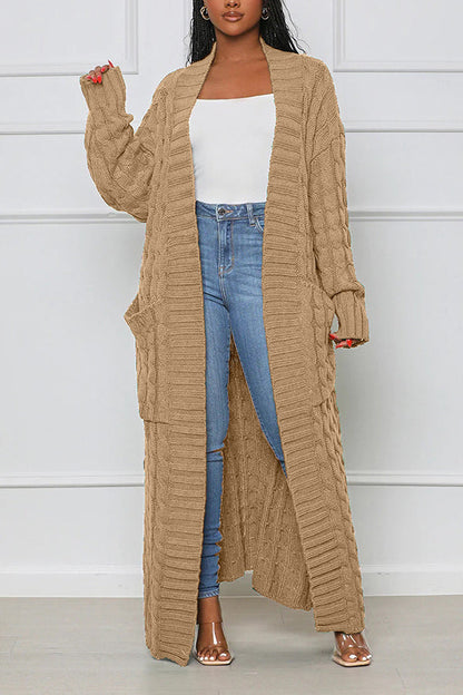 Frau trägt langen, beige Strick-Cardigan mit Zopfmuster, kombiniert mit weißem Top und blauer Jeans. Modetrend, Damenmode, Herbstoutfit.
