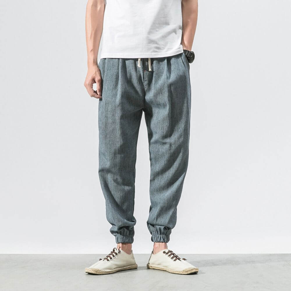 Herren Jogginghose aus grauem Leinen, lässiger Stil, kombiniert mit weißem T-Shirt und Espadrilles. Bequem und modisch für Freizeitkleidung.