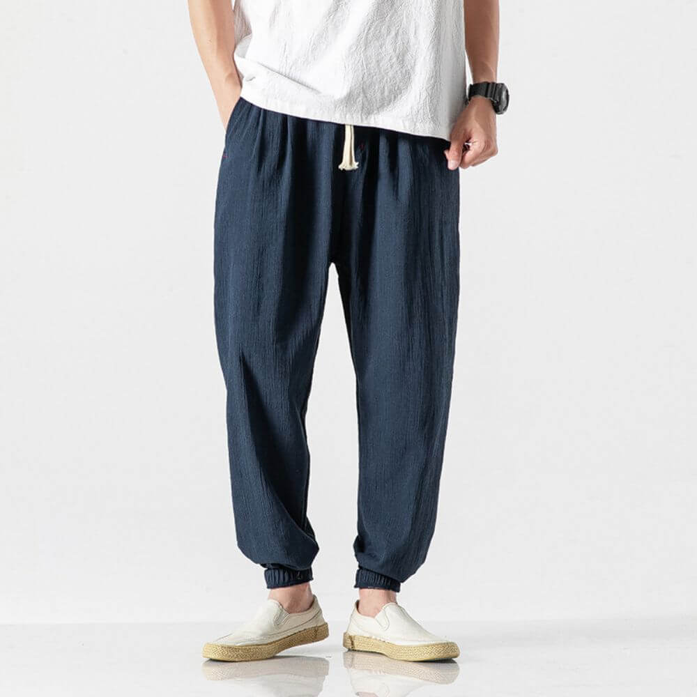Mann trägt dunkelblaue Leinenhose, weißes T-Shirt und weiße Schuhe. Modischer Freizeitlook, ideal für Sommer und Alltag.