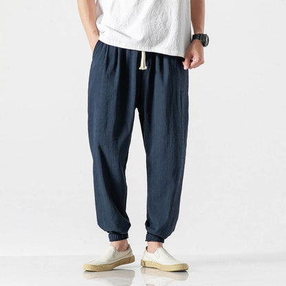Mann trägt dunkelblaue Leinenhose, weißes T-Shirt und weiße Schuhe. Modischer Freizeitlook, ideal für Sommer und Alltag.