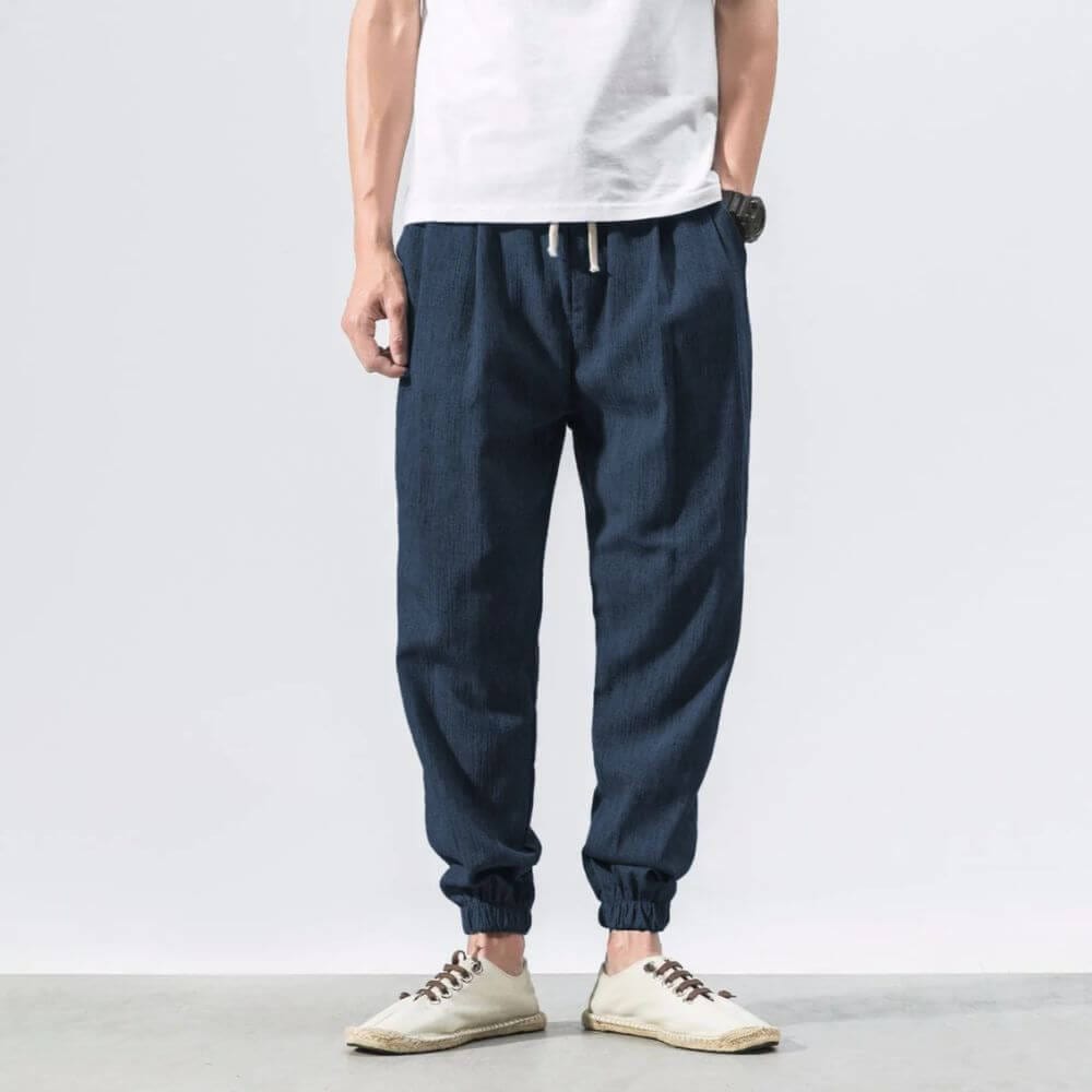 Mann trägt blaue Jogginghose und weiße Sneakers, lässiger Stil, Mode für Herren, bequeme Freizeitkleidung, moderne Herrenmode.
