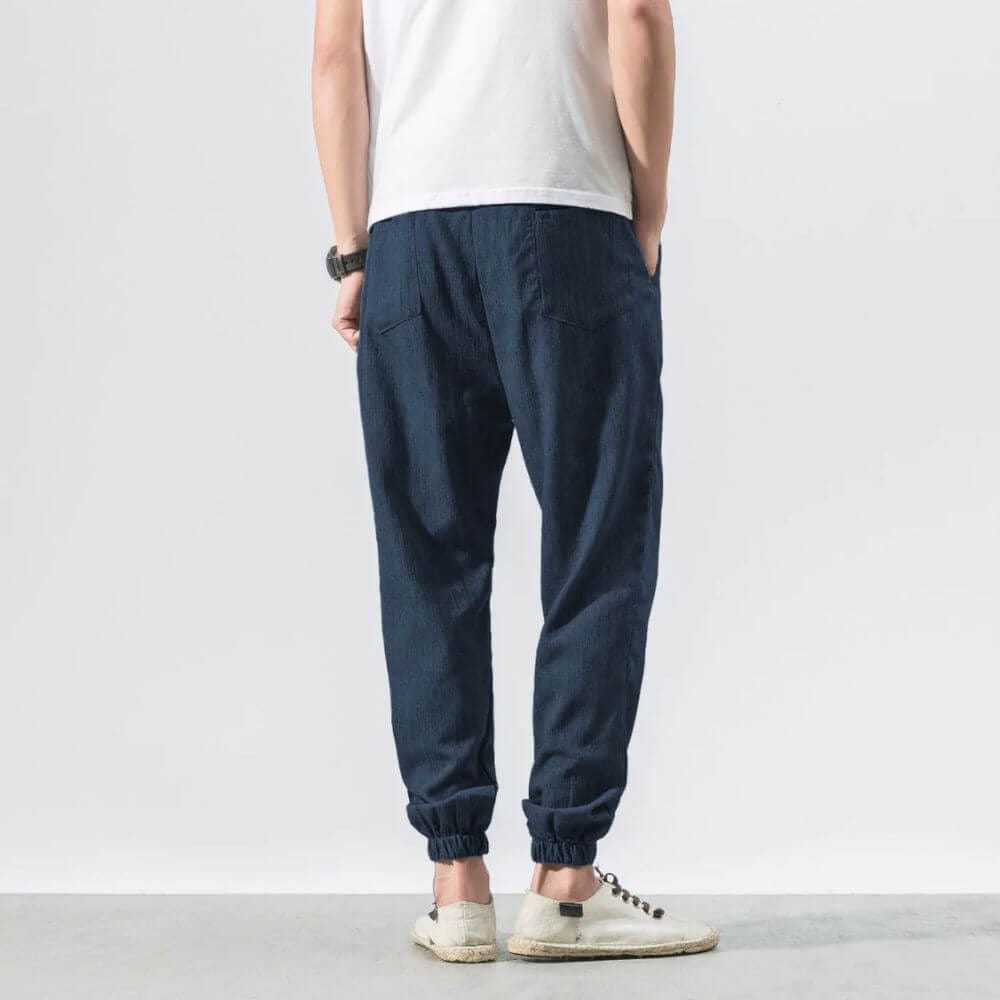 Rückansicht eines Mannes in blauer Jogginghose und weißem T-Shirt, lässiger Stil, weiße Sneaker, moderne Herrenmode, Freizeitkleidung.