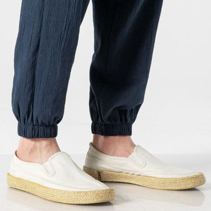 Weiße Espadrilles-Schuhe aus Segeltuch mit Bastsohle, getragen von einer Person in dunkelblauen Hosen. Ideal für Sommermode und Freizeitkleidung.