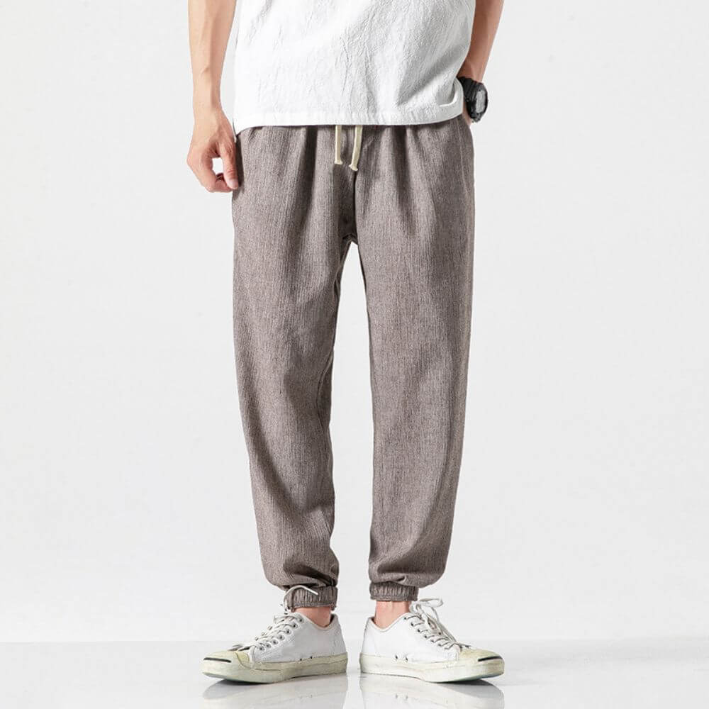 Mann in grauer Jogginghose und weißem T-Shirt, trägt weiße Sneaker. Lässige Herrenmode, bequeme Freizeitkleidung, moderner Stil.