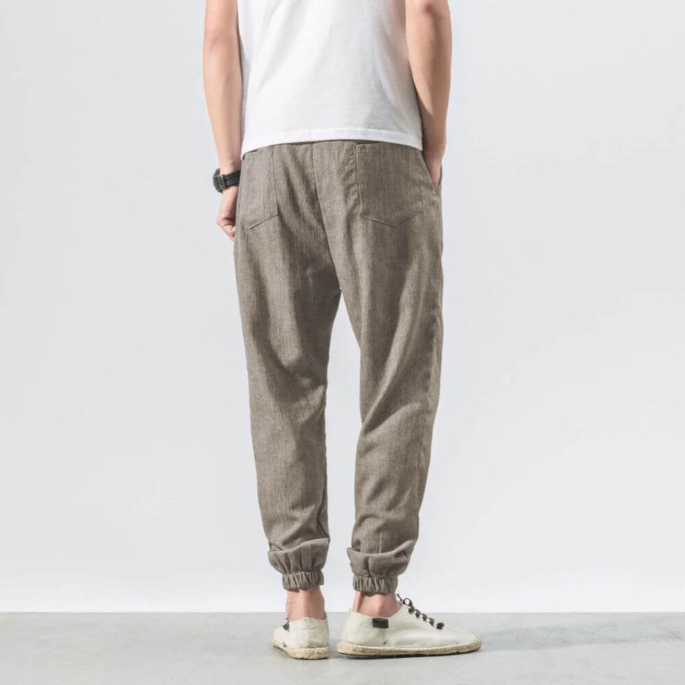Herrenmode: Rückansicht einer Person in beigen Leinenjogginghosen und weißen Sneakers. Lässiger Stil, ideal für Freizeit und Komfort.