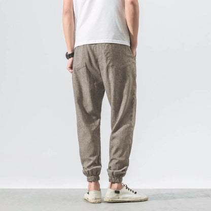 Herrenmode: Rückansicht einer Person in beigen Leinenjogginghosen und weißen Sneakers. Lässiger Stil, ideal für Freizeit und Komfort.