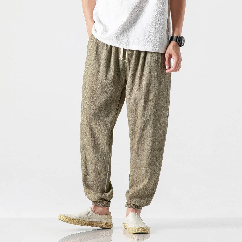 Herren Leinenhose in Beige, locker geschnitten, mit elastischem Bund und Kordelzug. Kombiniert mit weißem T-Shirt und Armbanduhr.