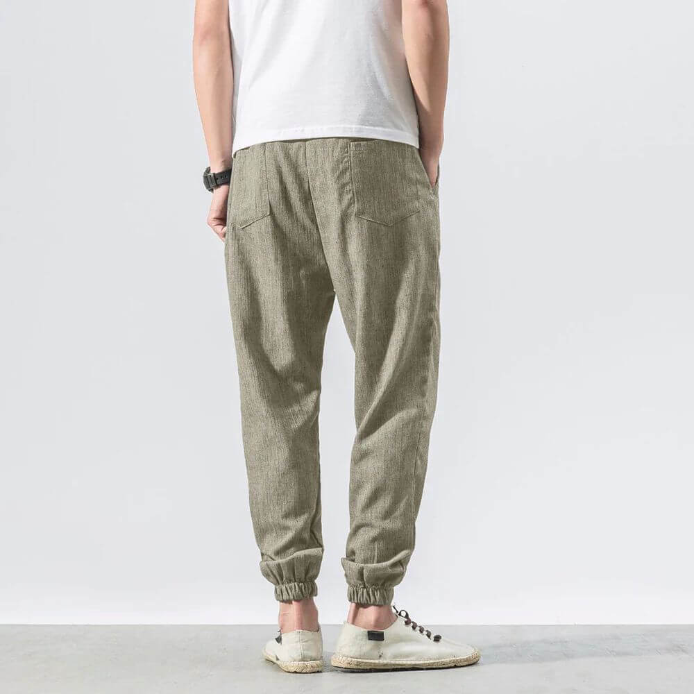 Rückansicht eines Mannes in beiger Leinenhose und weißem T-Shirt, lässiger Stil, weiße Sneaker, minimalistisch, modisch, komfortabel.