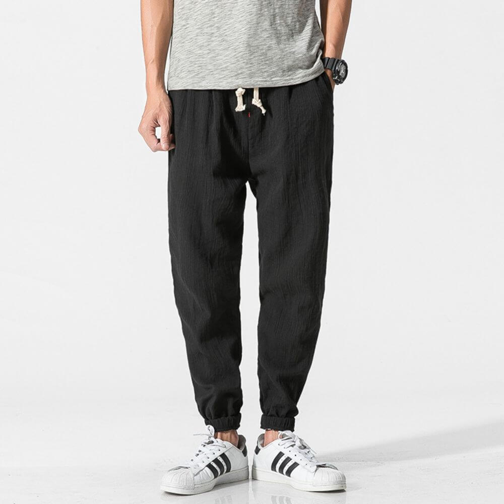 Mann trägt schwarze Jogginghose und graues T-Shirt, kombiniert mit weißen Adidas-Sneakern. Bequeme Freizeitmode für Herren.