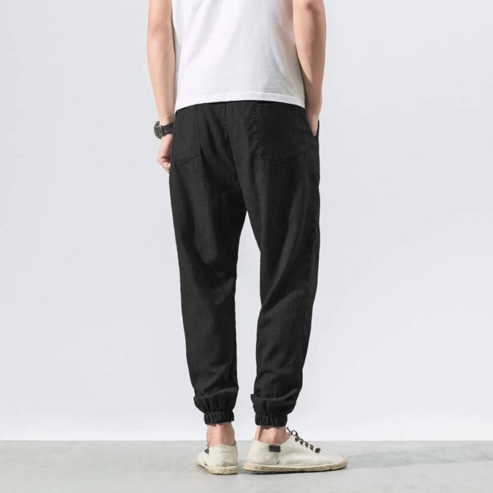 Rückansicht einer Person in schwarzer Jogginghose und weißem T-Shirt, trägt weiße Sneaker. Lässige Mode, Herrenbekleidung, Freizeitlook.