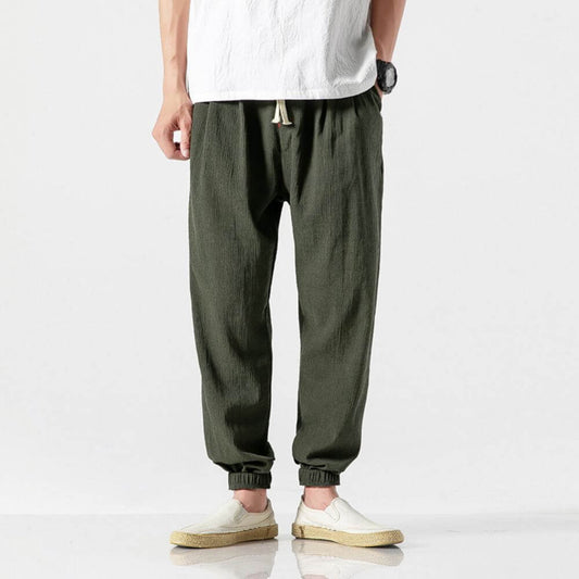 Grüne Leinenhose für Herren, lässig geschnitten, kombiniert mit weißen Espadrilles und weißem T-Shirt. Ideal für Sommermode und Freizeitkleidung.