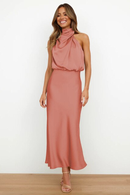Frau in elegantem, rosafarbenem Abendkleid mit Halterneck-Design, lächelnd, stehend auf Holzboden, Mode, Damenbekleidung, Abendmode.