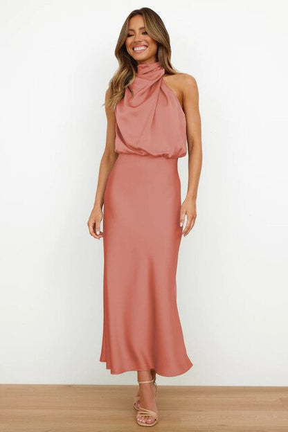 Frau in elegantem, rosafarbenem Abendkleid mit Halterneck-Design, lächelnd, stehend auf Holzboden, Mode, Damenbekleidung, Abendmode.