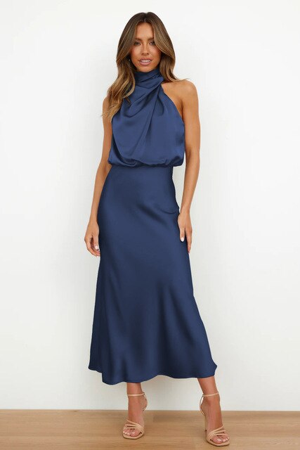 Frau in elegantem, blauem Satinkleid mit hohem Kragen und ärmellosem Design, stehend vor weißem Hintergrund, trägt beige High Heels.
