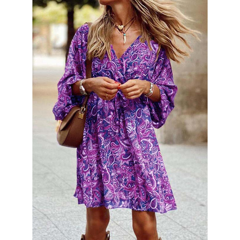 Frau in lila geblümtem Kleid, trägt braune Tasche und Schmuck, steht draußen. Modetrend, Sommerkleid, lässiger Stil, Damenmode.