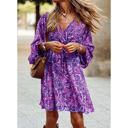 Frau in lila geblümtem Kleid, trägt braune Tasche und Schmuck, steht draußen. Modetrend, Sommerkleid, lässiger Stil, Damenmode.