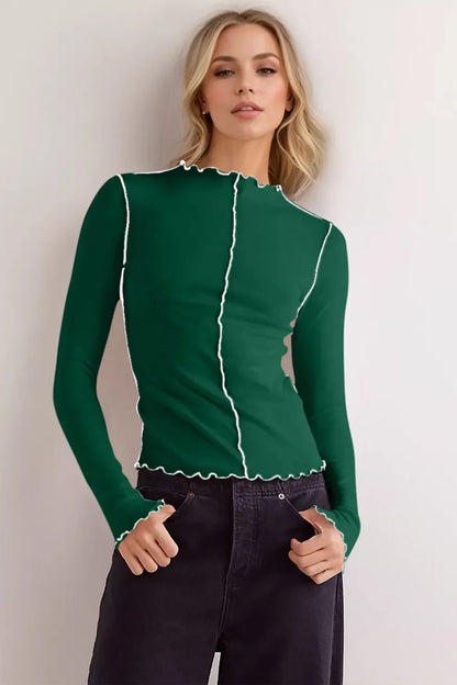 Frau in grünem, langärmligem Oberteil mit weißen Nähten, schwarze Hose, lässiger Look, Mode, Damenbekleidung, stilvoll, modern.