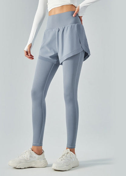 Frau in grauen Sportleggings mit Shorts und weißen Sneakers, ideal für Fitness und Yoga. Sportbekleidung für Damen, bequem und modisch.