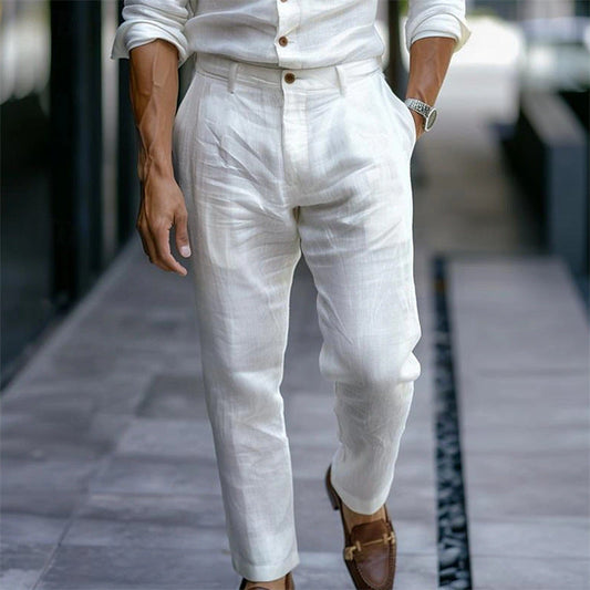 Mann in weißem Leinenanzug und braunen Loafers auf Gehweg. Elegante Herrenmode, Sommeroutfit, stilvolle Kleidung, Freizeitlook.