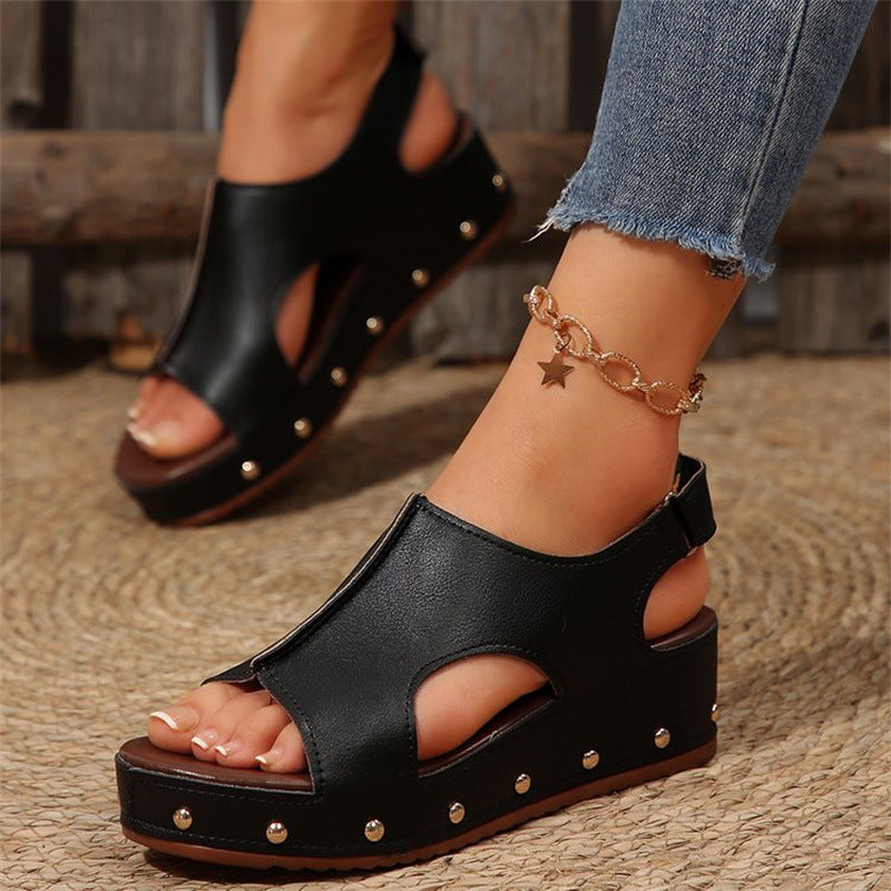 Schwarze Plateau-Sandalen mit Nieten, getragen mit Jeans und einem goldenen Stern-Armband. Modische Damen-Sommerschuhe, ideal für Freizeitoutfits.