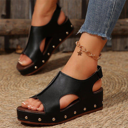 Schwarze Plateau-Sandalen mit Nieten, getragen mit Jeans und einem goldenen Stern-Armband. Modische Damen-Sommerschuhe, ideal für Freizeitoutfits.