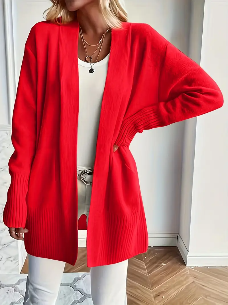Frau in rotem Strickcardigan, weißem Top und Hose. Modetrend, Damenmode, Herbstoutfit, stilvoll, lässig, elegantes Design, gemütlicher Look.