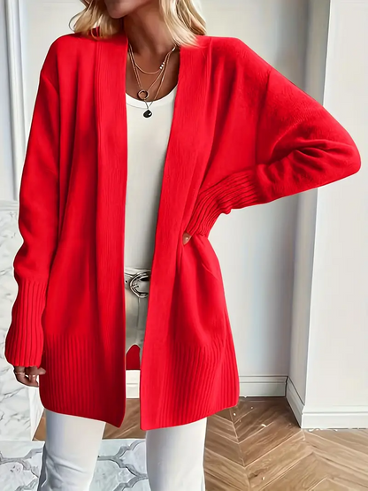 Frau in rotem Strickcardigan, weißem Top und Hose. Modetrend, Damenmode, Herbstoutfit, stilvoll, lässig, elegantes Design, gemütlicher Look.