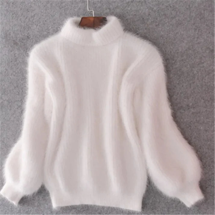 Weiße flauschige Damenpullover aus Angorawolle mit langen Ärmeln und Rollkragen, hängend an einem Holzbügel vor grauem Hintergrund.