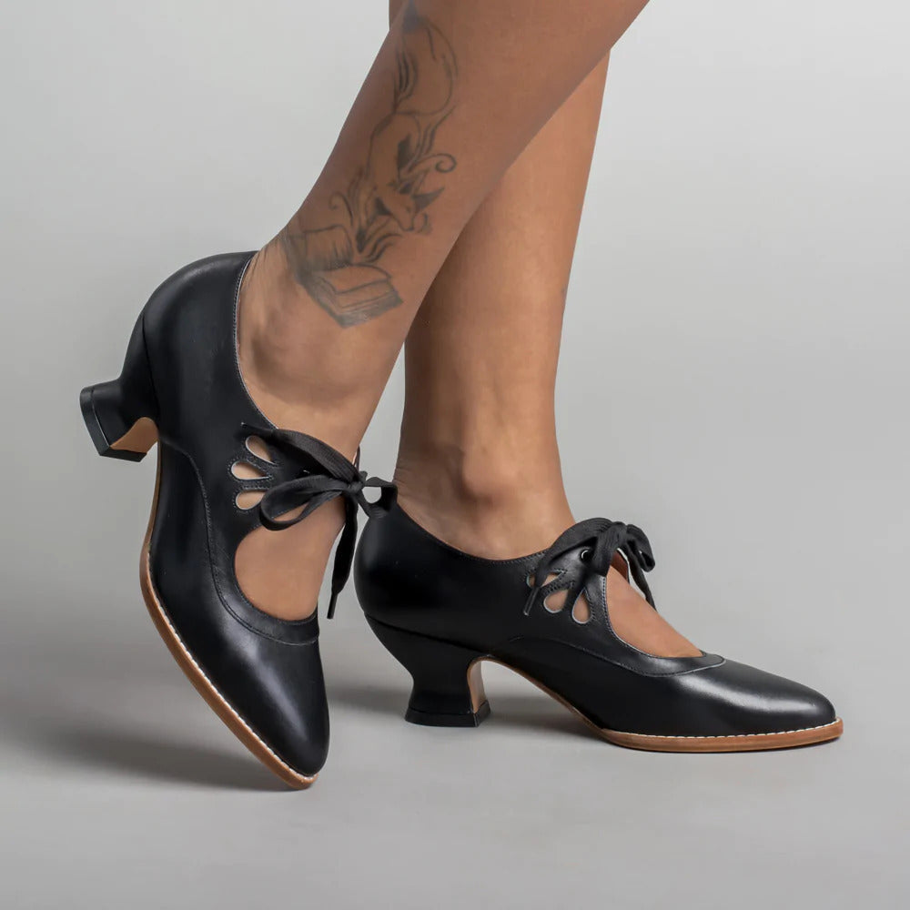 Schwarze Tanzschuhe mit Absatz und Schnürung, getragen von tätowierten Beinen. Elegante Damen-Tanzschuhe, ideal für Salsa oder Tango.