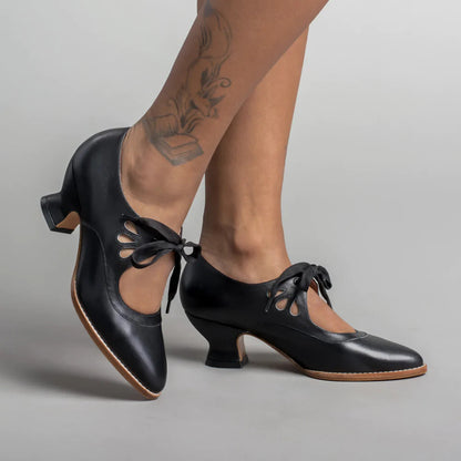 Schwarze Tanzschuhe mit Absatz und Schnürung, getragen von tätowierten Beinen. Elegante Damen-Tanzschuhe, ideal für Salsa oder Tango.