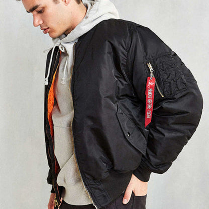 Junger Mann in schwarzer Bomberjacke mit rotem Schlüsselanhänger, grauem Hoodie und schwarzer Hose. Modetrend, Streetwear, lässiger Stil.