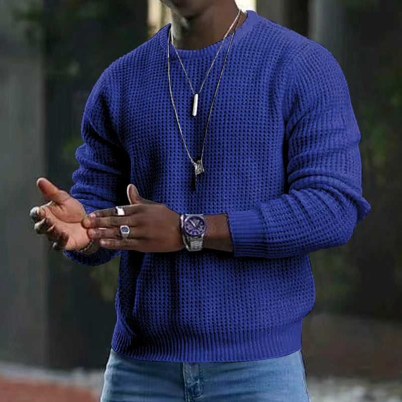 Mann in blauem Strickpullover, trägt Armbanduhr und Halsketten, gestikuliert mit Händen. Mode, Herrenbekleidung, Accessoires.