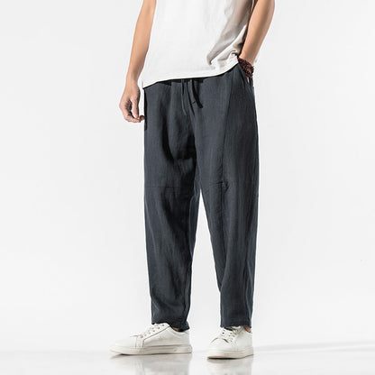 Mann in lässiger, dunkelgrauer Leinenhose und weißem T-Shirt, trägt weiße Sneaker. Moderne Herrenmode, bequeme Freizeitkleidung.