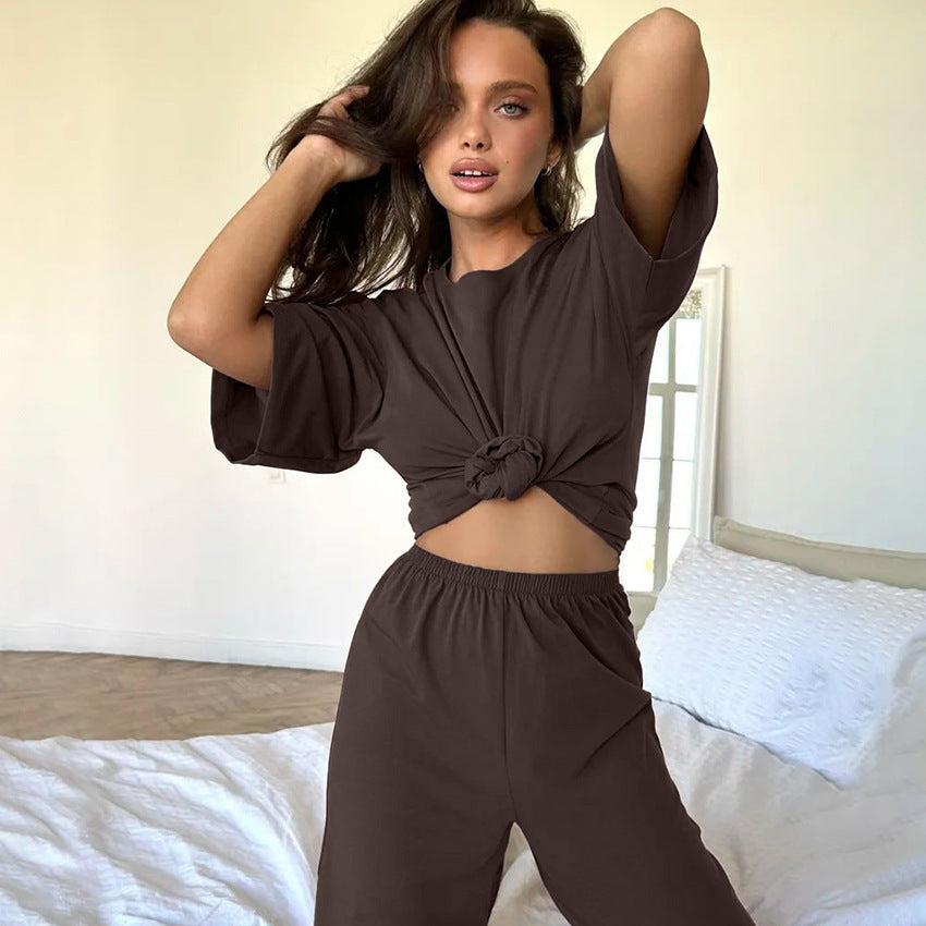 Frau in braunem, geknotetem T-Shirt und Hose posiert im Schlafzimmer. Modetrend, lässiger Look, Damenbekleidung, Freizeitoutfit.